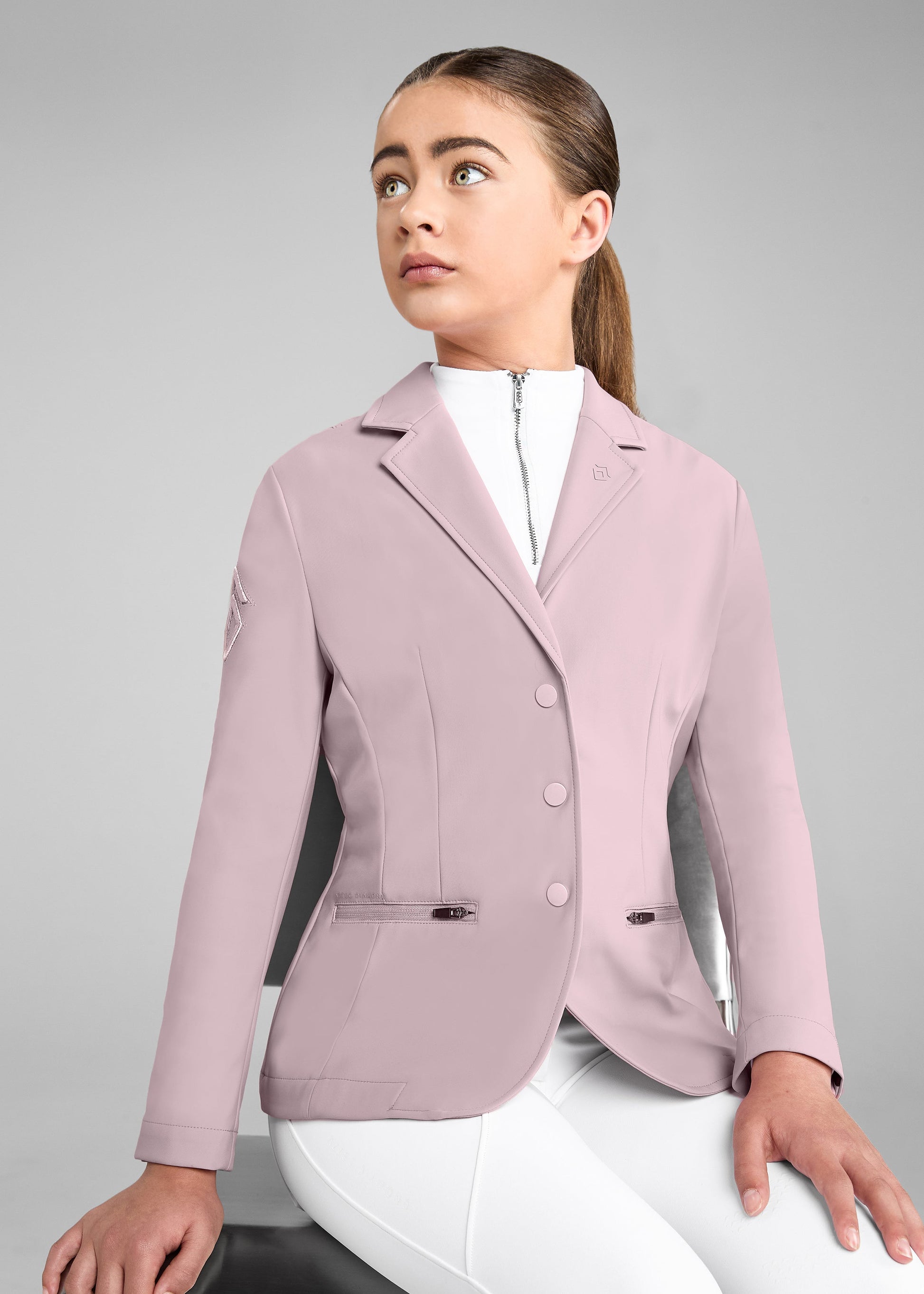 Woman wearing a light pink equestrian jacket on a gray background