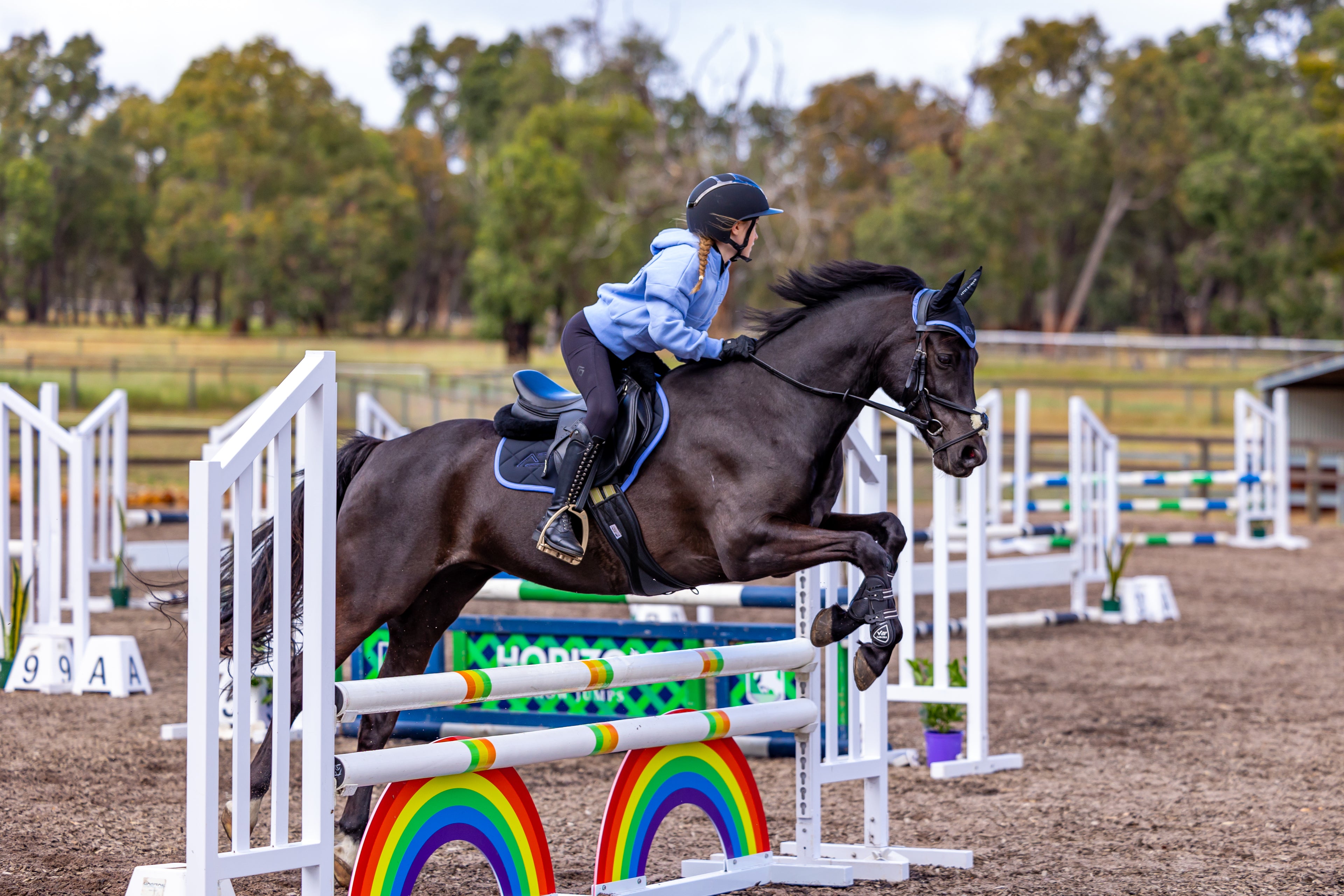 Horse and rider jumping over a rainbow-colored jump in an equestrian arena.